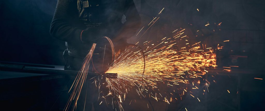 Young man grinding metal on steel pipe with flash sparks